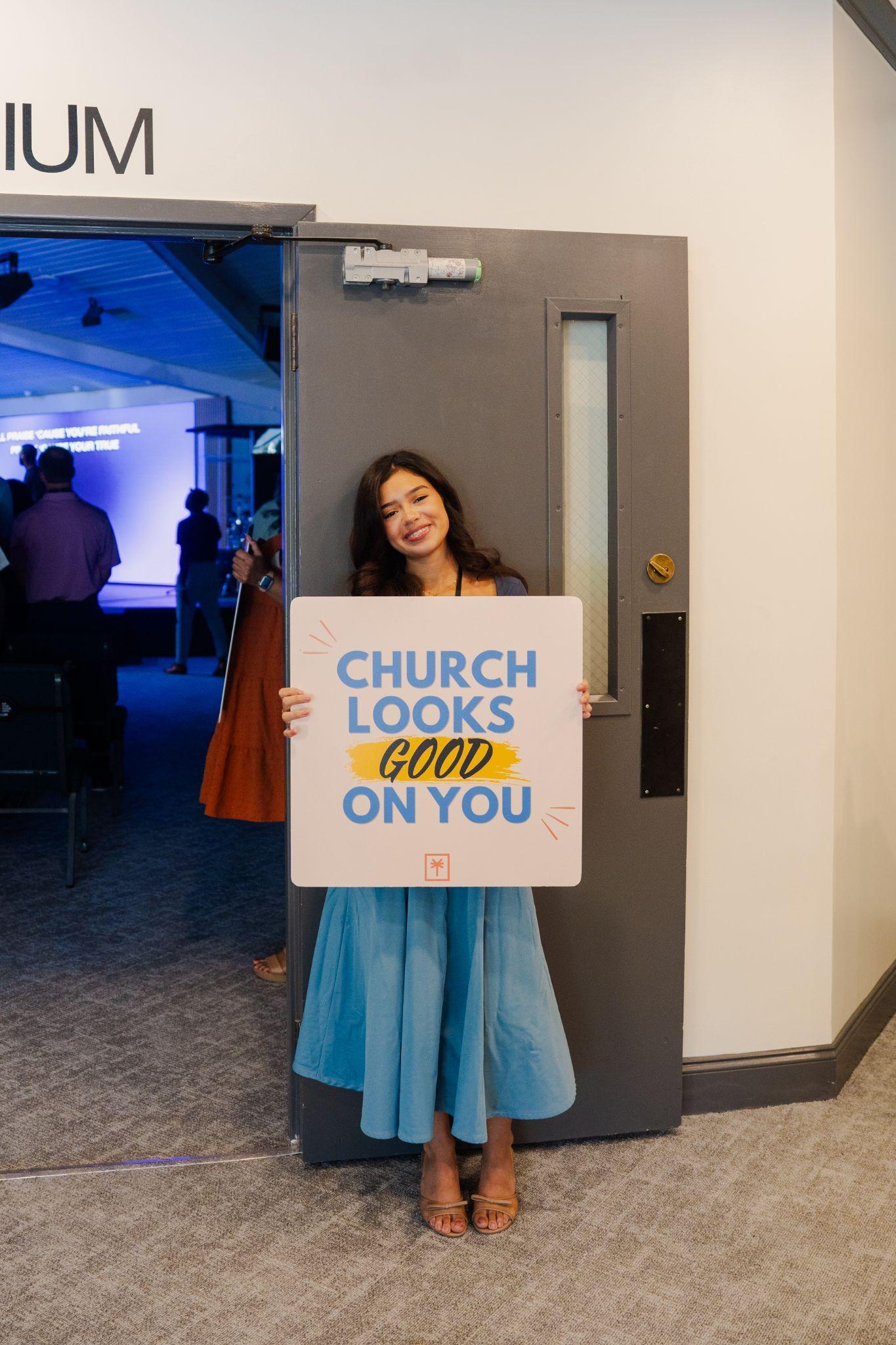 A LIIV volunteer holding a Church Looks Good on You welcome sign